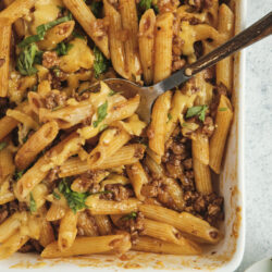 Ground Beef Casserole with penne pasta, melted cheese, and fresh basil in a baking dish.