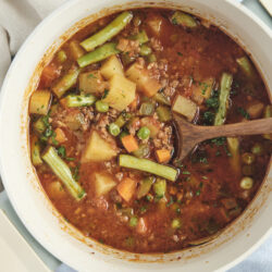 Hamburger Soup simmering in a white pot with ground beef, potatoes, and mixed vegetables.