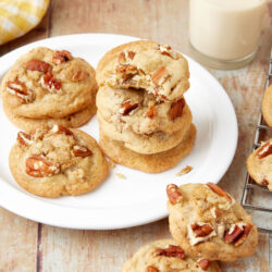 Praline Cookies with chopped pecans, stacked on a white plate with a glass of milk.