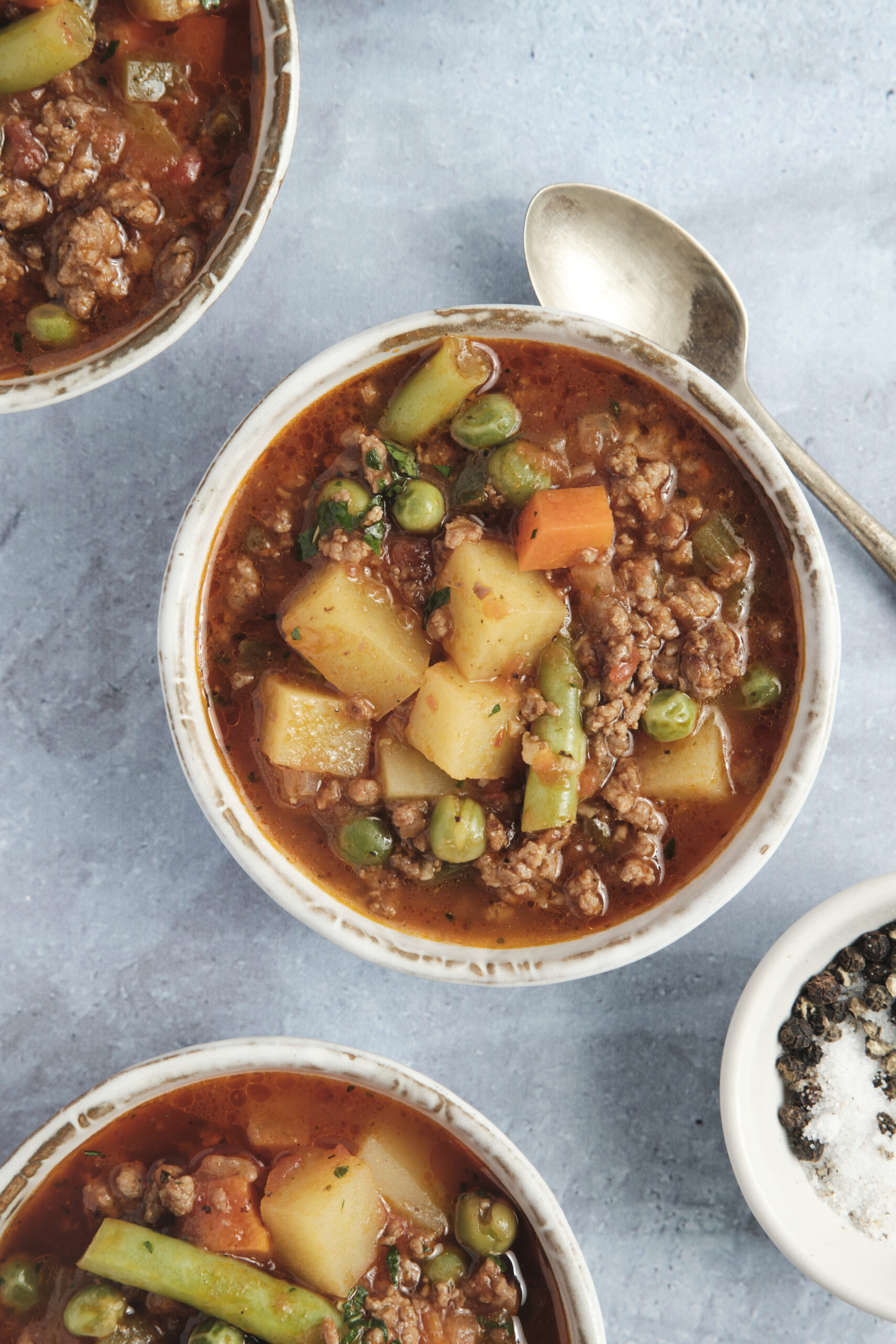 Bowls of Hamburger Soup with ground beef, potatoes, mixed vegetables, and parsley.