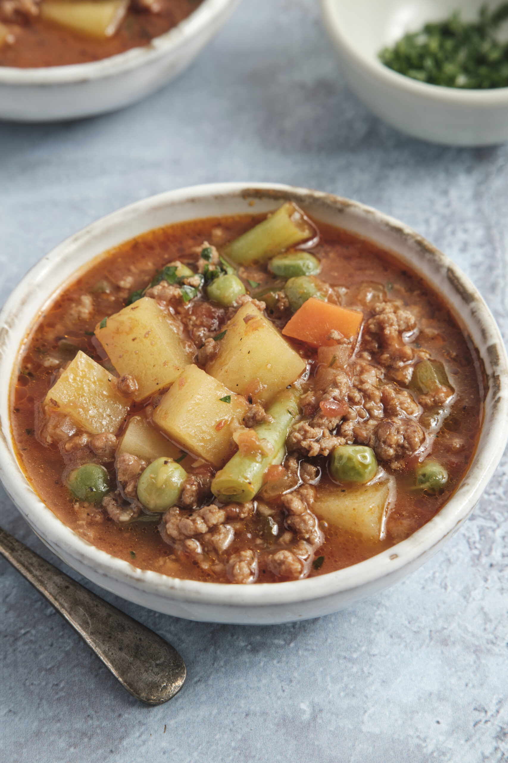 A bowl of hamburger soup with ground beef, potatoes, mixed vegetables, and fresh parsley.