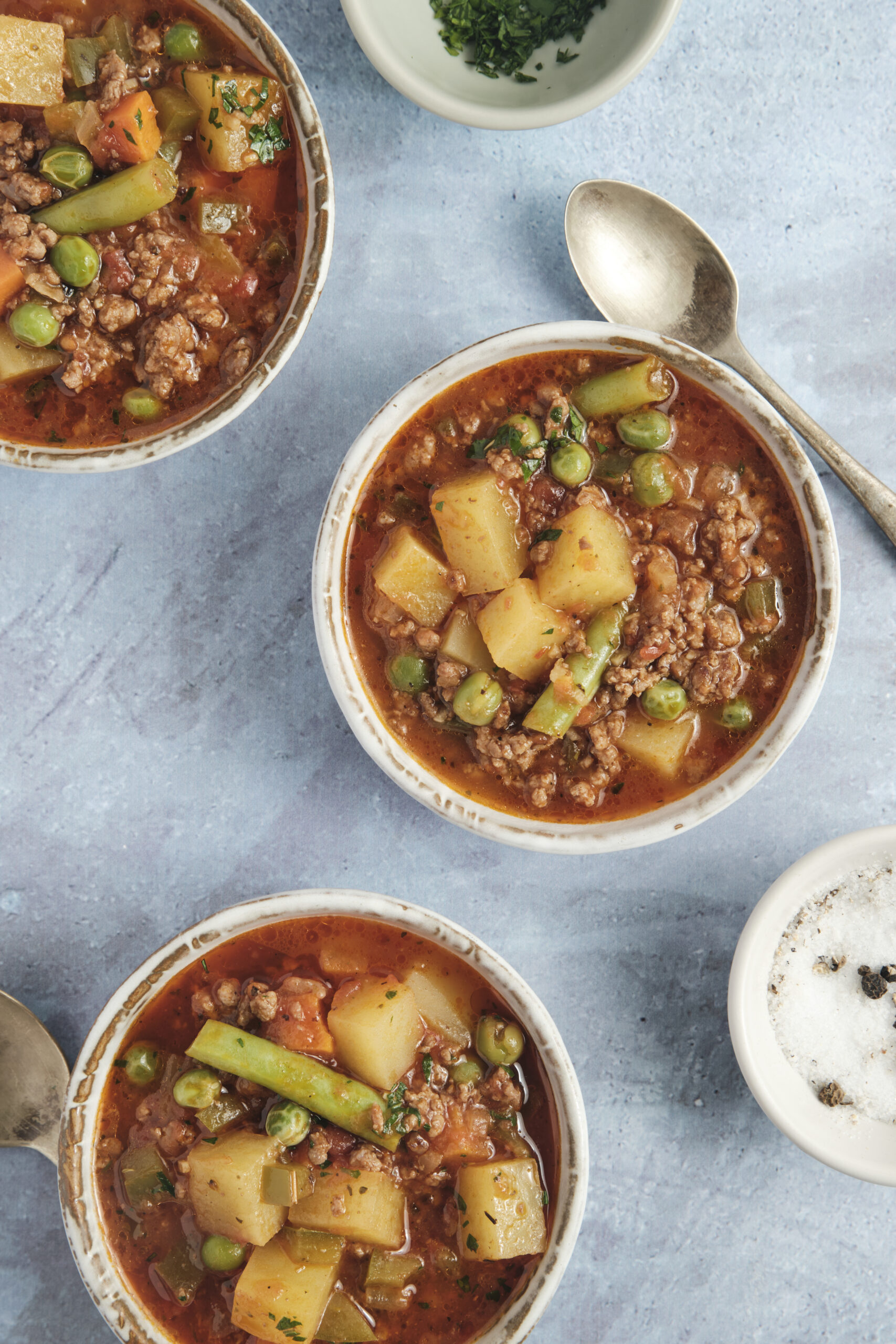 Three bowls of hearty Hamburger Soup with ground beef, potatoes, peas, and green beans.
