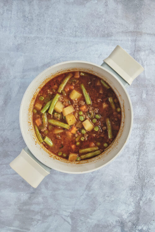 Hamburger soup simmering in a pot with ground beef and vegetables.