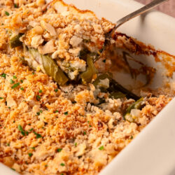 Asparagus casserole with a golden cracker and Parmesan topping, being served from a white dish.