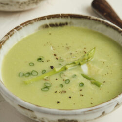 Creamy asparagus soup in a rustic bowl, garnished with asparagus spears, chives, and black pepper.