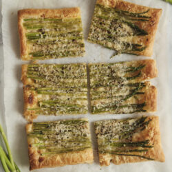 Slices of golden Asparagus Tart with asparagus spears, grated Parmesan, and black pepper.