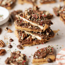 Christmas Crack pieces stacked on parchment paper, topped with chocolate, pecans, and festive sprinkles.