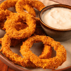 Crispy keto onion rings on a plate with a side of creamy keto-friendly dipping sauce.