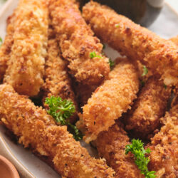 Golden-brown mozzarella sticks on a plate, garnished with parsley and served with marinara sauce.