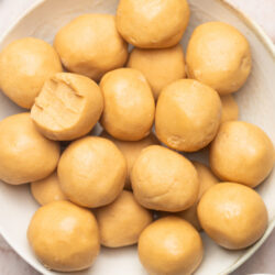 No-bake peanut butter balls in a white bowl, one broken open, with peanut butter.