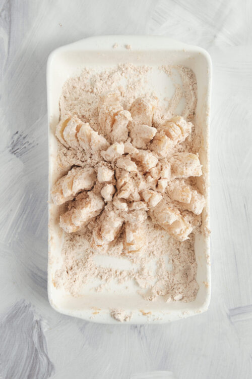Coating a blooming onion in a seasoned flour mixture.