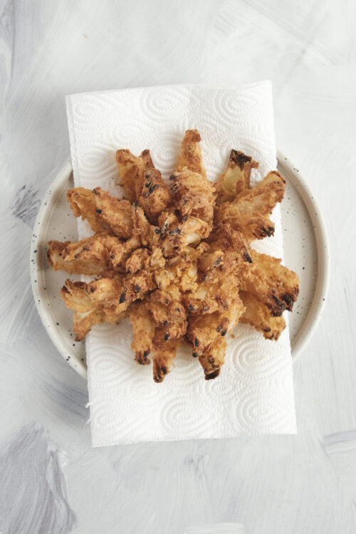 A crispy, golden blooming onion draining on paper towels.