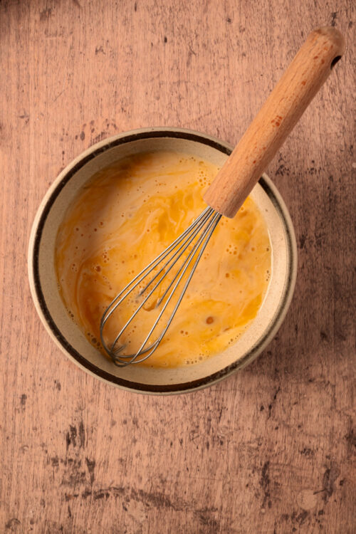 Whisking eggs and heavy cream in a bowl for keto onion rings.