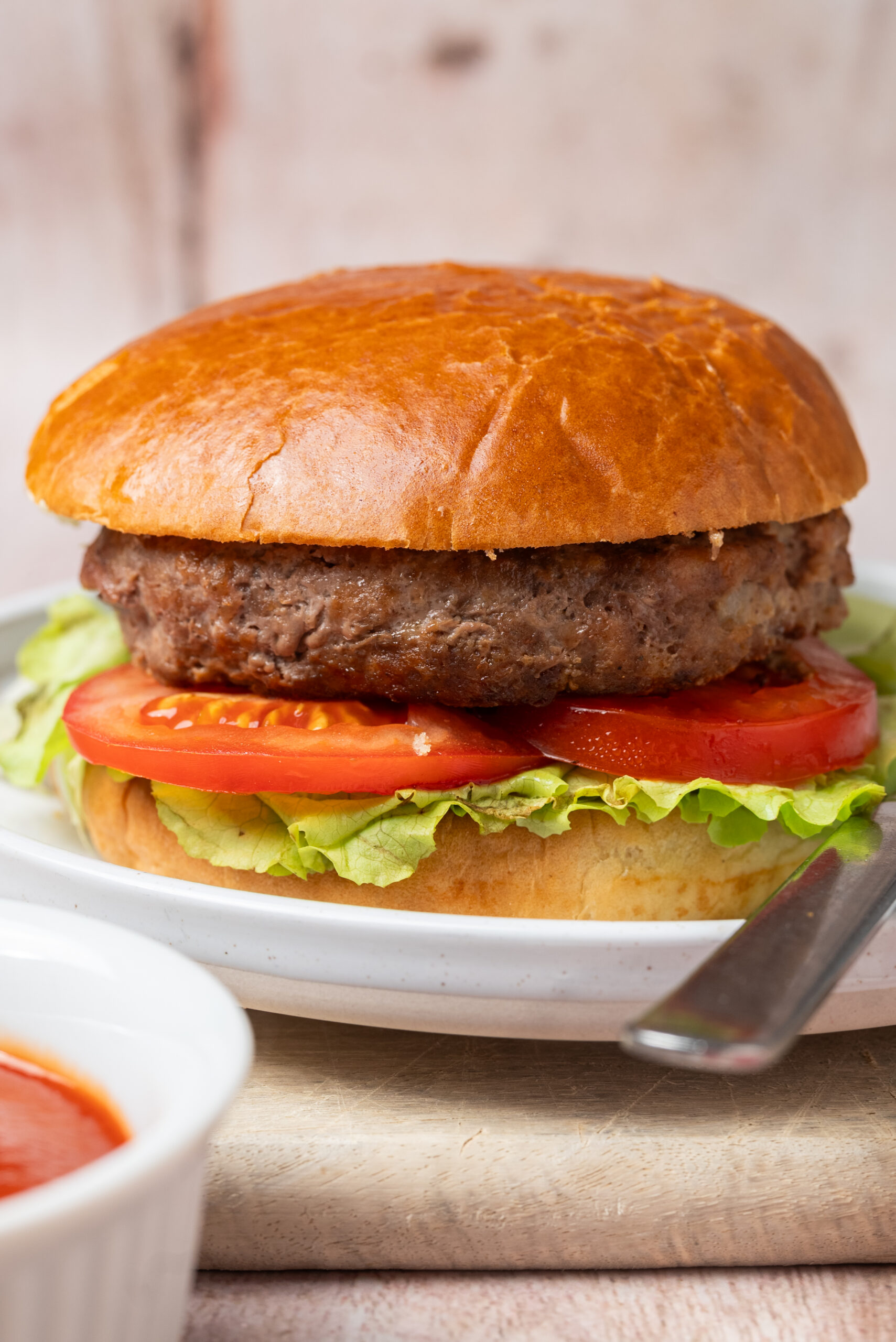 A meatloaf burger with lettuce and tomato on a bun, served with ketchup.