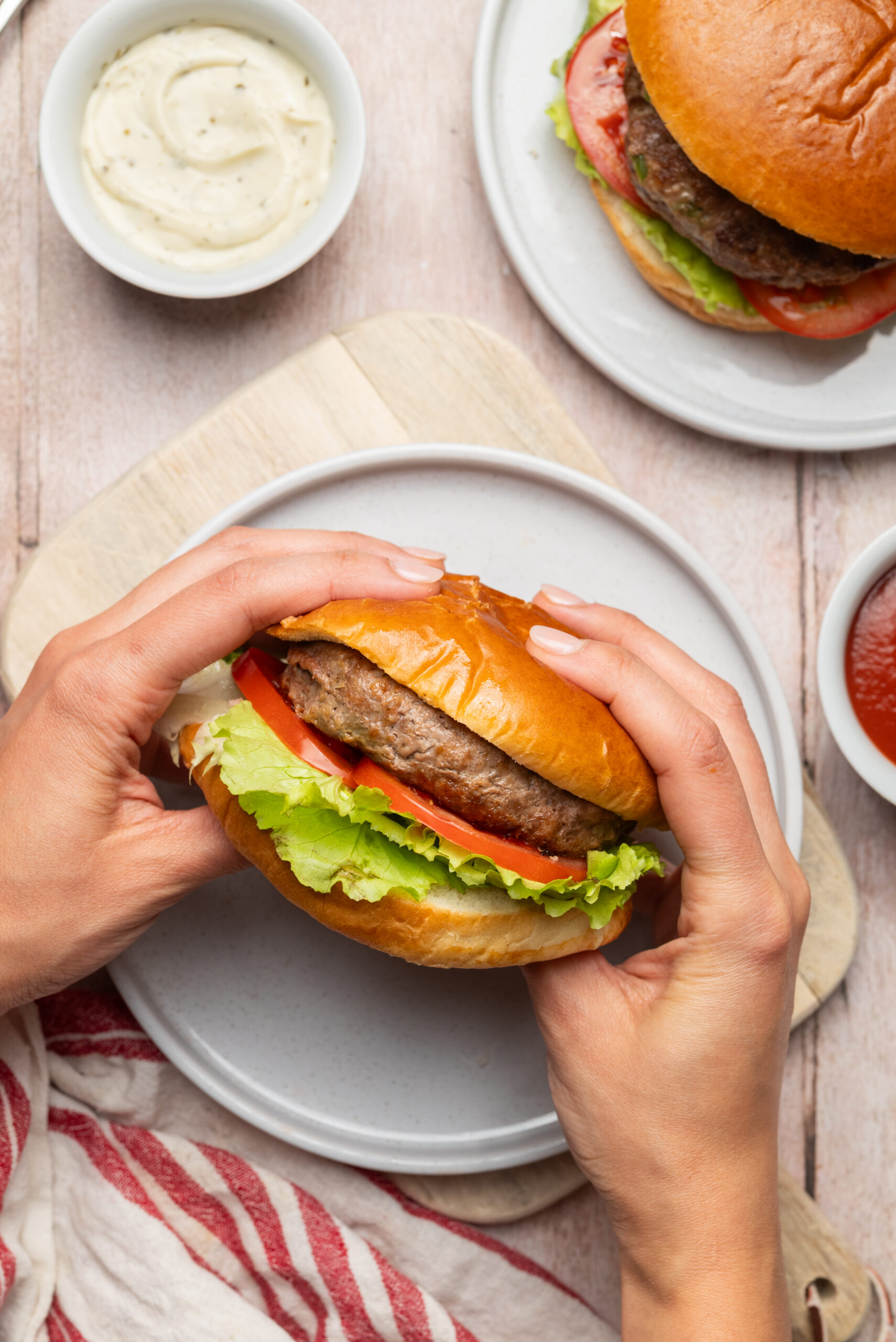 A person holding a Meatloaf Burger with lettuce and tomato on a bun.
