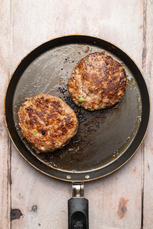 Two Meatloaf Burger patties browning in a nonstick skillet.