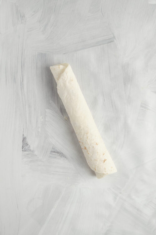 Rolling a flour tortilla tightly for Mexican Tortilla Roll-Ups.