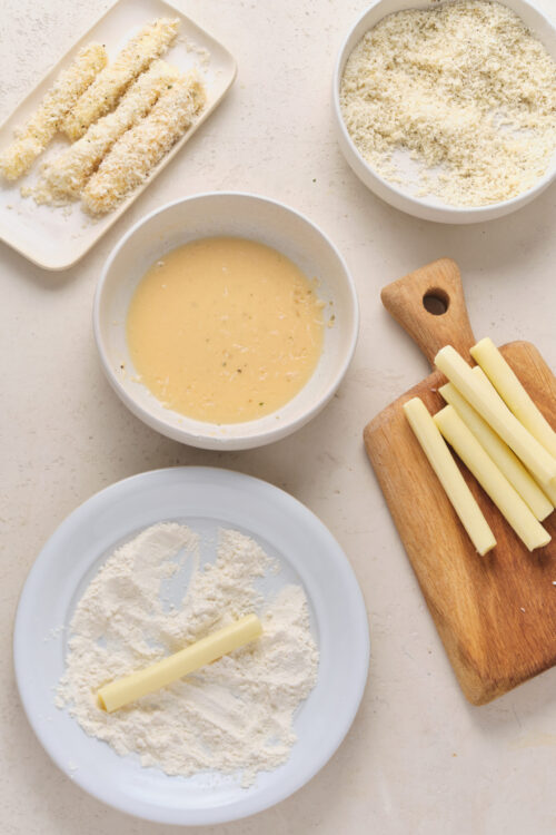 Dipping mozzarella sticks in flour, egg mixture, and panko breadcrumbs.