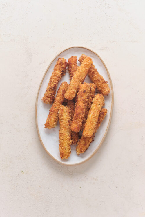 Golden-brown breaded mozzarella sticks on a white oval plate.