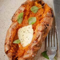 Air-fryer baked sweet potato, split open, topped with butter, pepper, and fresh basil.