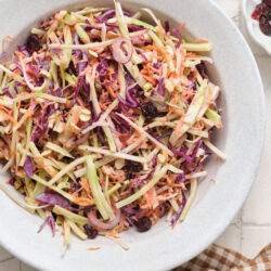 Broccoli slaw in a white bowl, mixed with red onion, almonds, and dried cranberries.