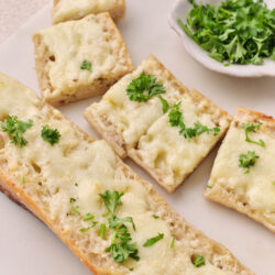 Slices of cheesy garlic bread topped with melted mozzarella and Parmesan, garnished with fresh parsley.