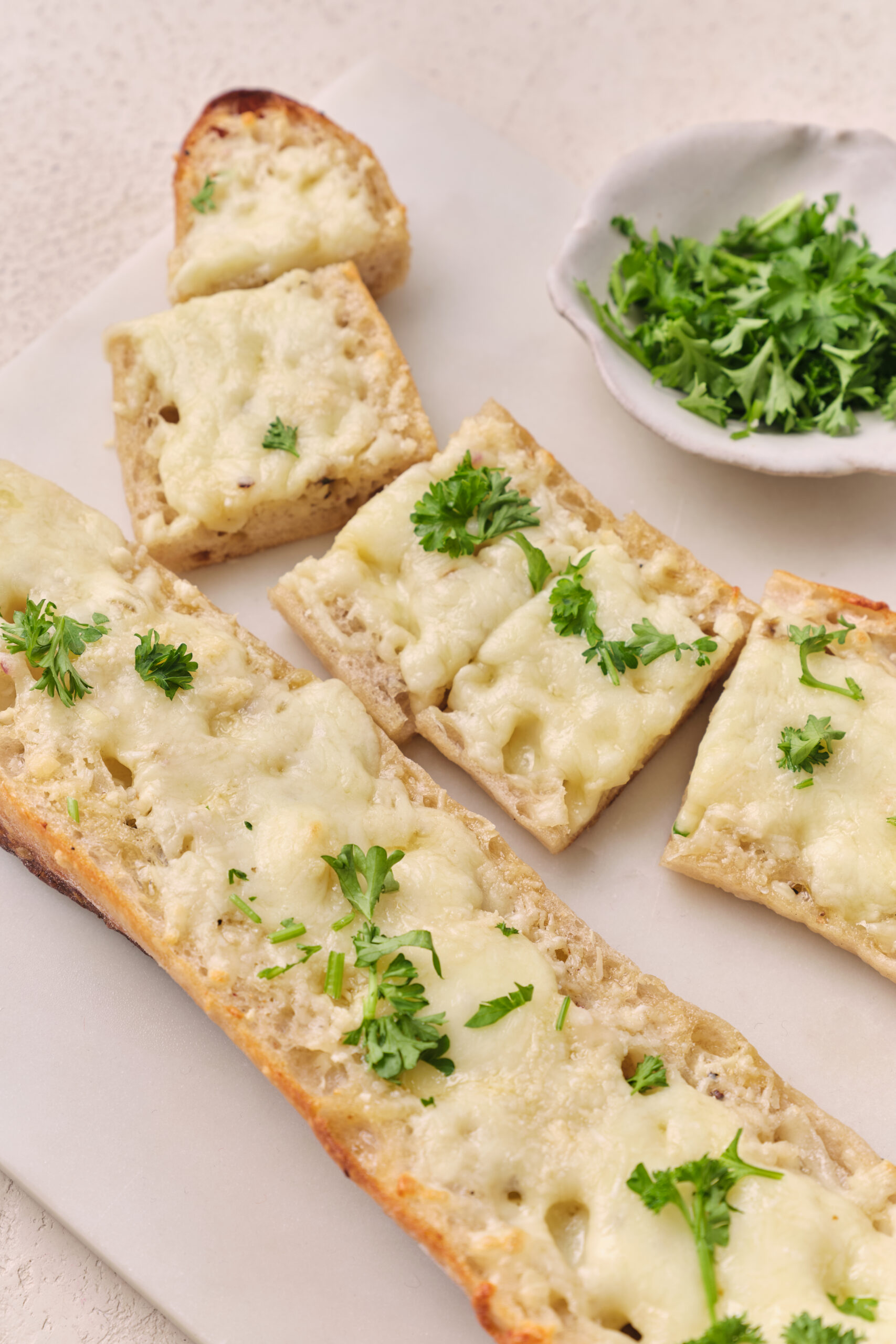 Slices of cheesy garlic bread topped with melted mozzarella and Parmesan, garnished with fresh parsley.