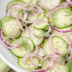 Cucumber and onion salad with thinly sliced red onions and fresh dill in a white bowl.