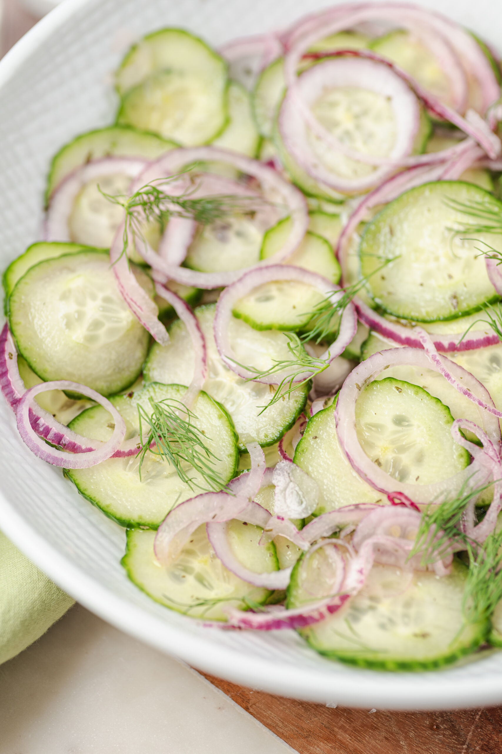 Cucumber and onion salad with thinly sliced red onions and fresh dill in a white bowl.