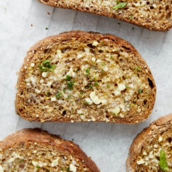 Slices of garlic toast spread with butter and minced garlic, garnished with fresh parsley.