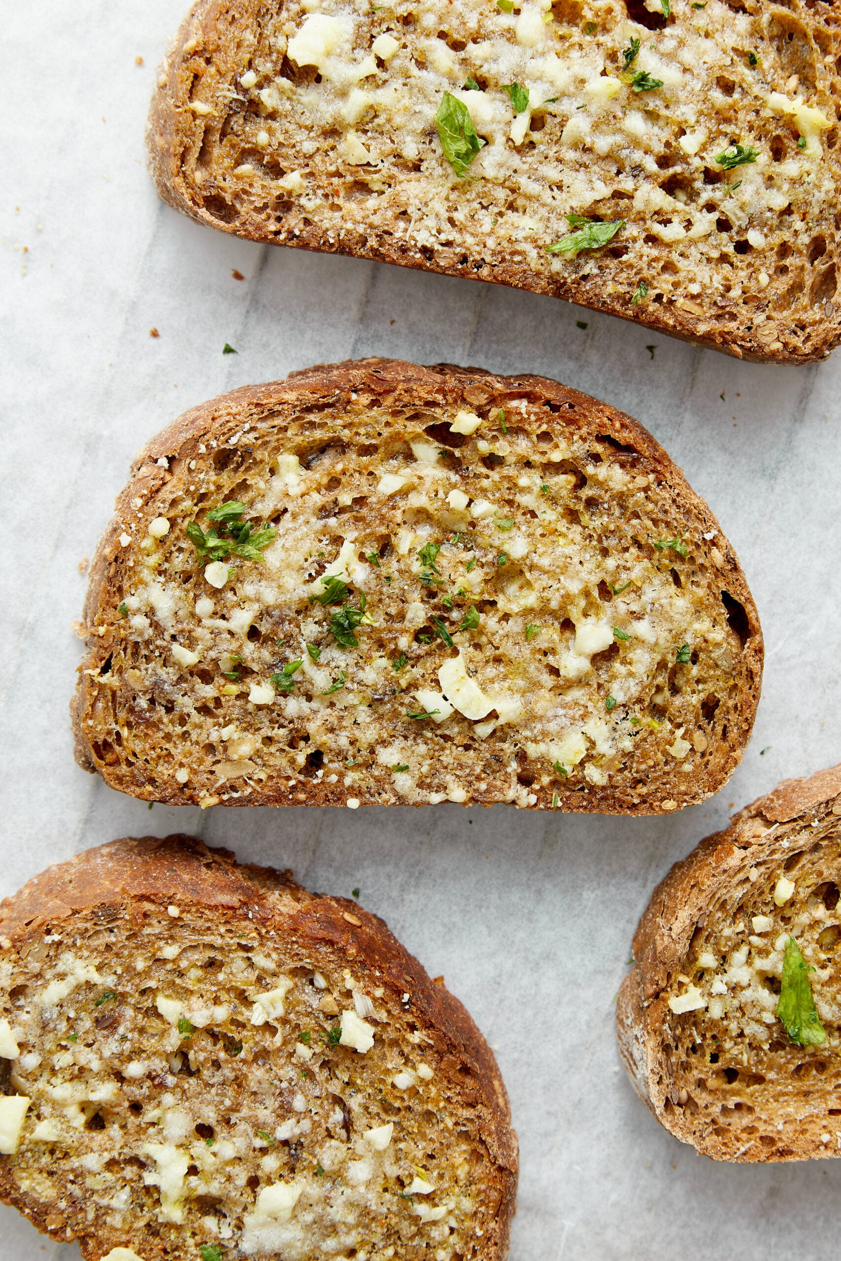 Slices of garlic toast spread with butter and minced garlic, garnished with fresh parsley.