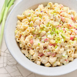 Creamy macaroni salad in a white bowl, topped with chopped green onions.