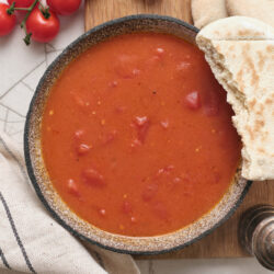 Tomato gravy in a bowl, served with pita bread and fresh cherry tomatoes.