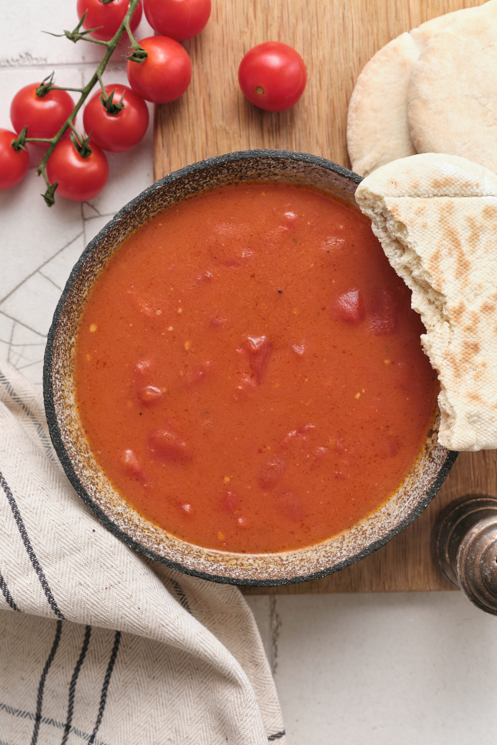 Tomato gravy in a bowl, served with pita bread and fresh cherry tomatoes.