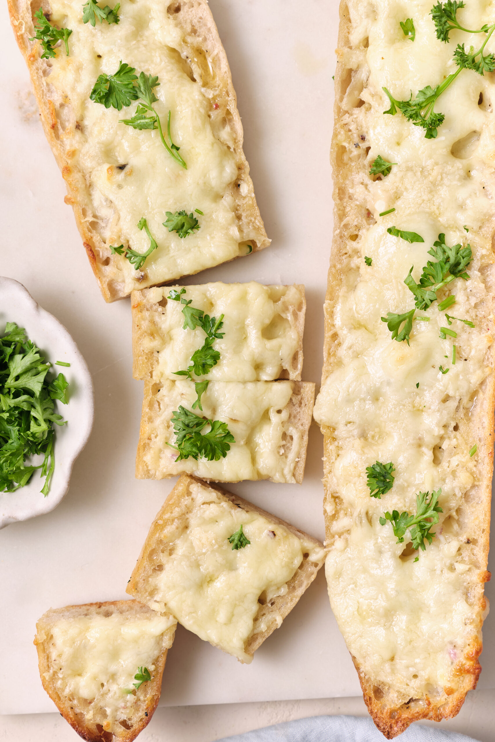 Cheesy garlic bread slices with melted mozzarella and Parmesan, garnished with fresh parsley.