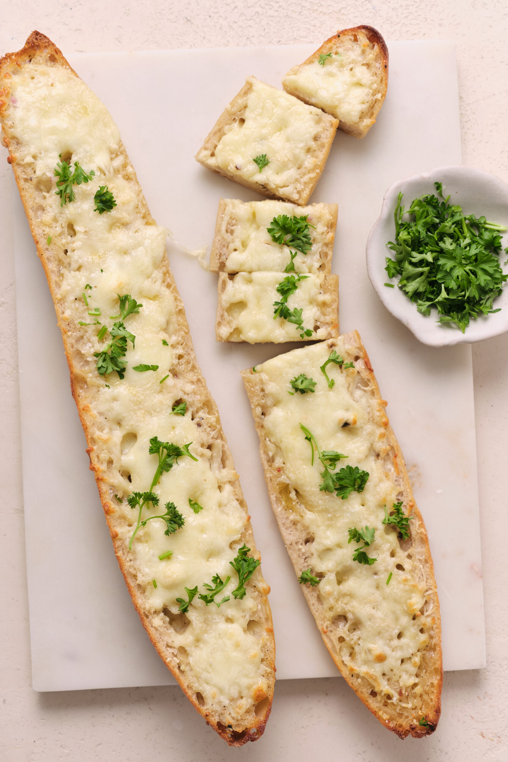 Cheesy Garlic Bread, sliced and garnished with fresh parsley on a white marble board.