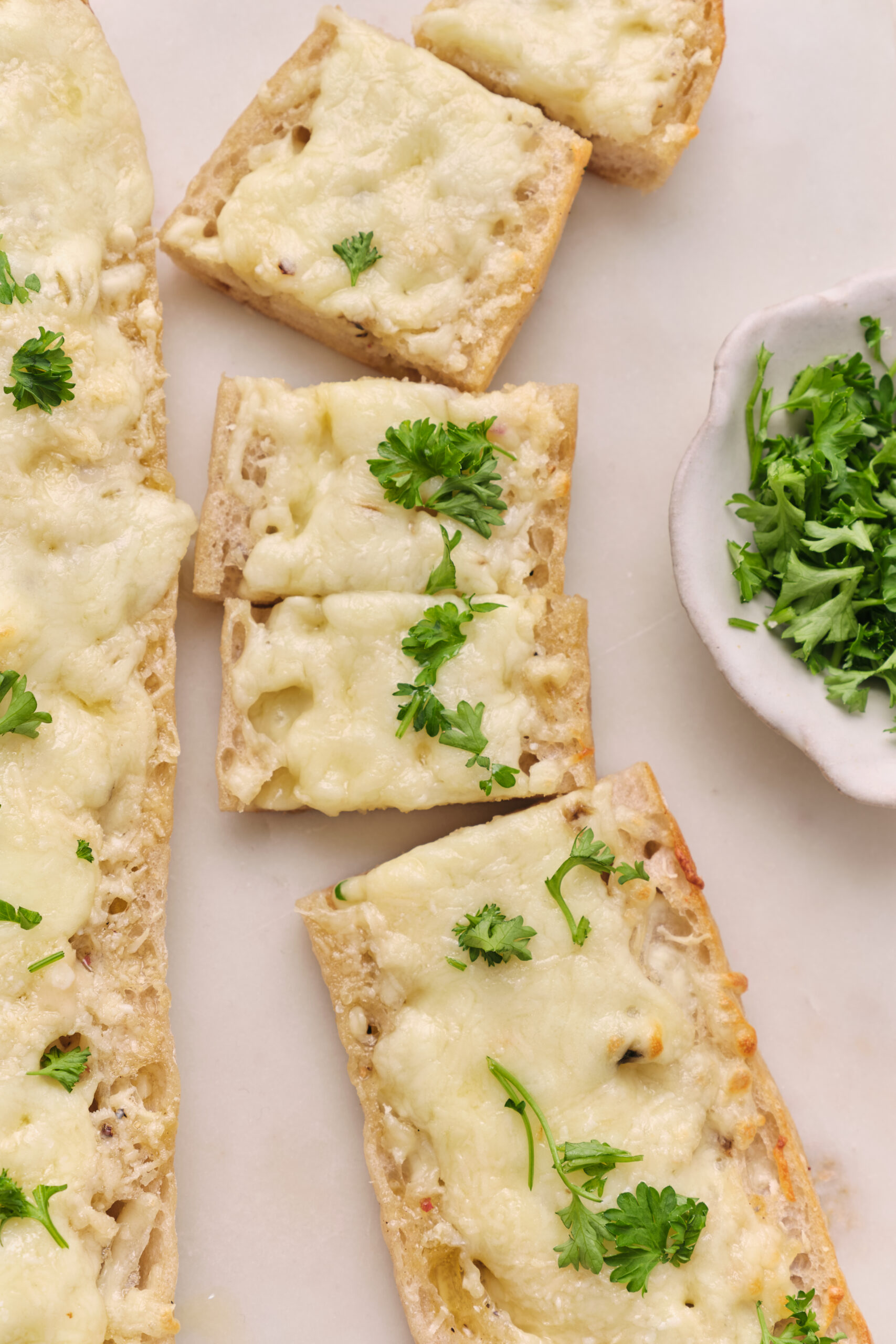 Cheesy garlic bread slices topped with melted mozzarella and Parmesan, garnished with fresh parsley.