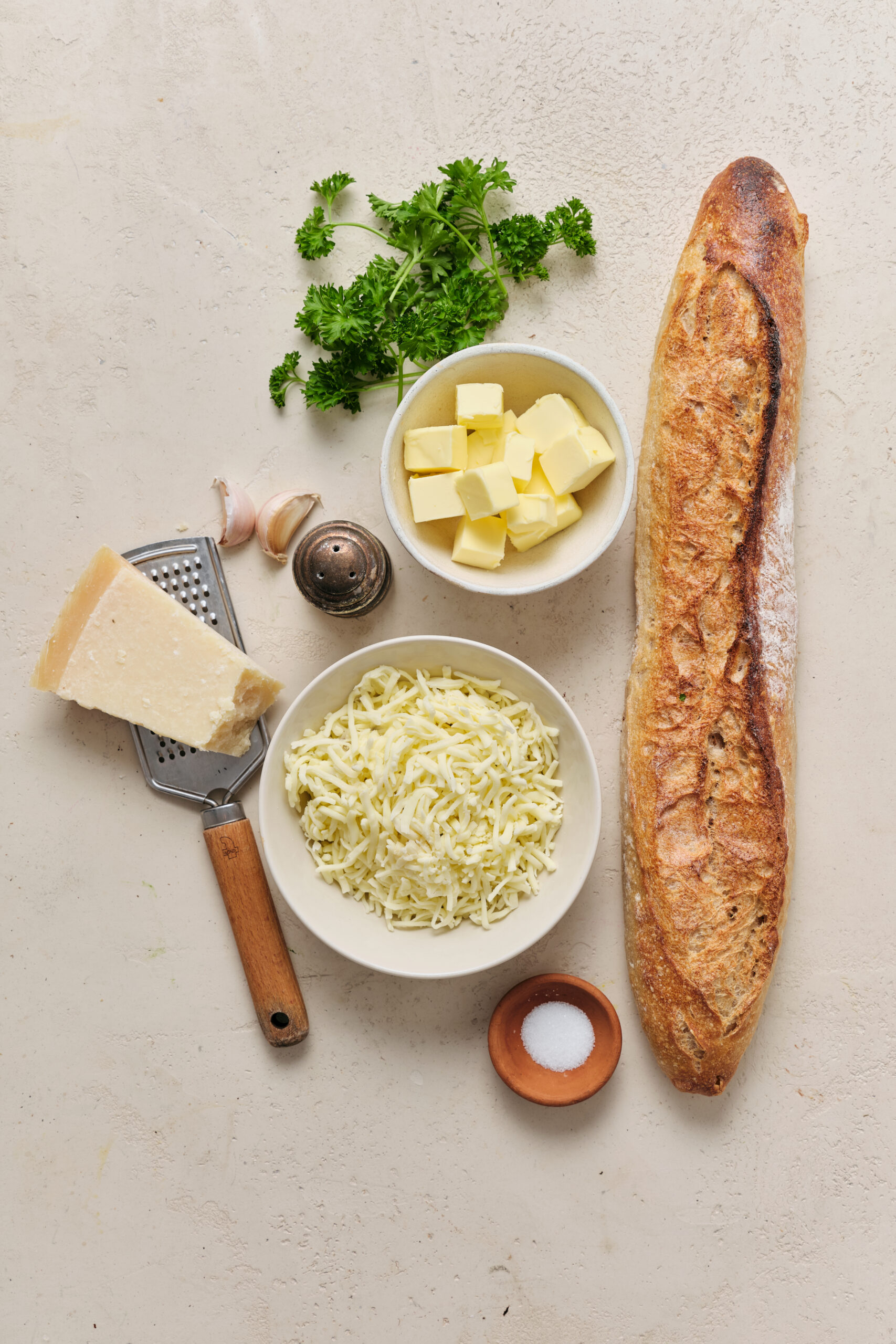 Ingredients for cheesy garlic bread: French bread, butter, garlic, shredded mozzarella, Parmesan, parsley, and salt.