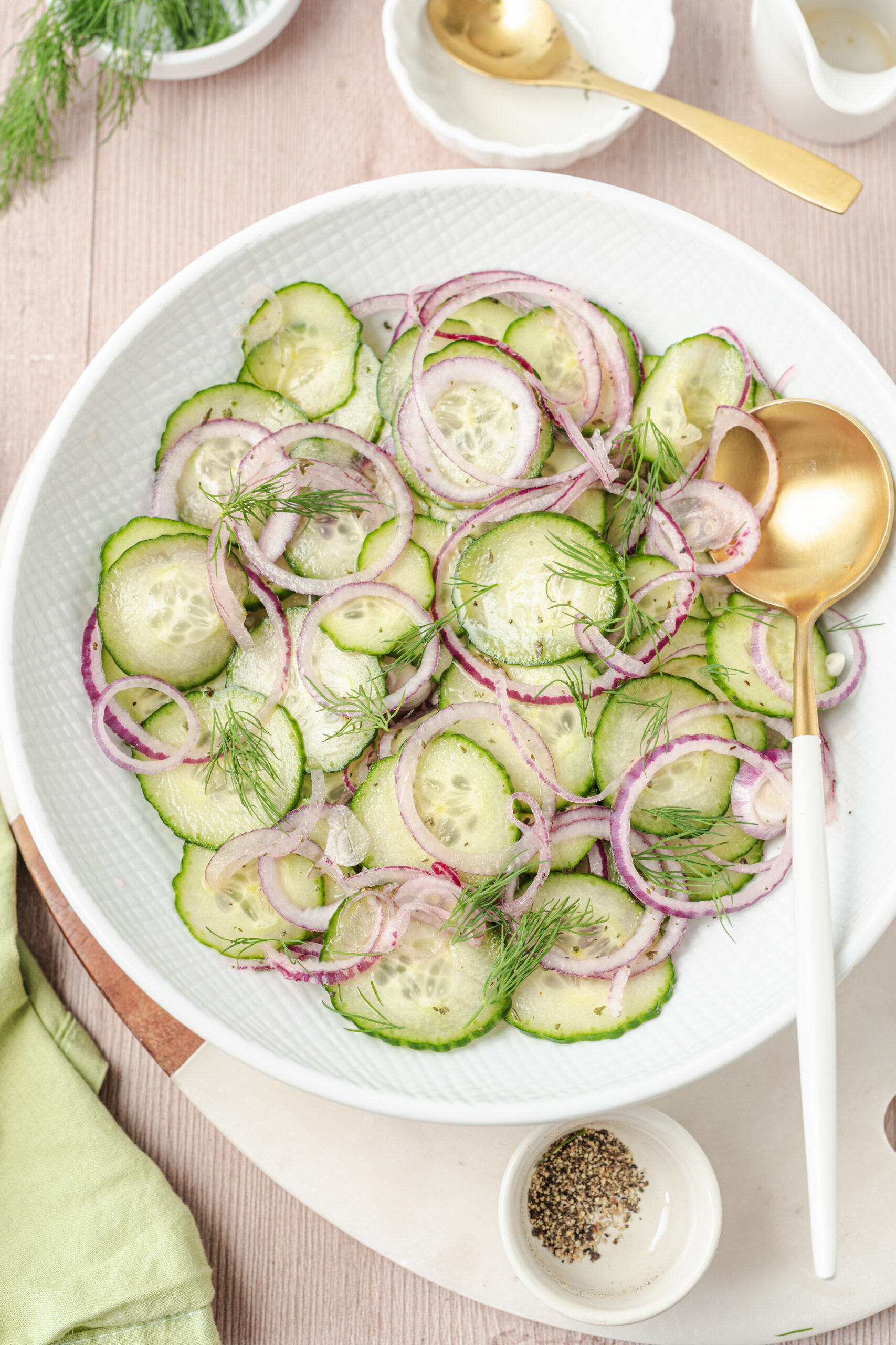 Cucumber and onion salad in a white bowl, garnished with fresh dill and black pepper.