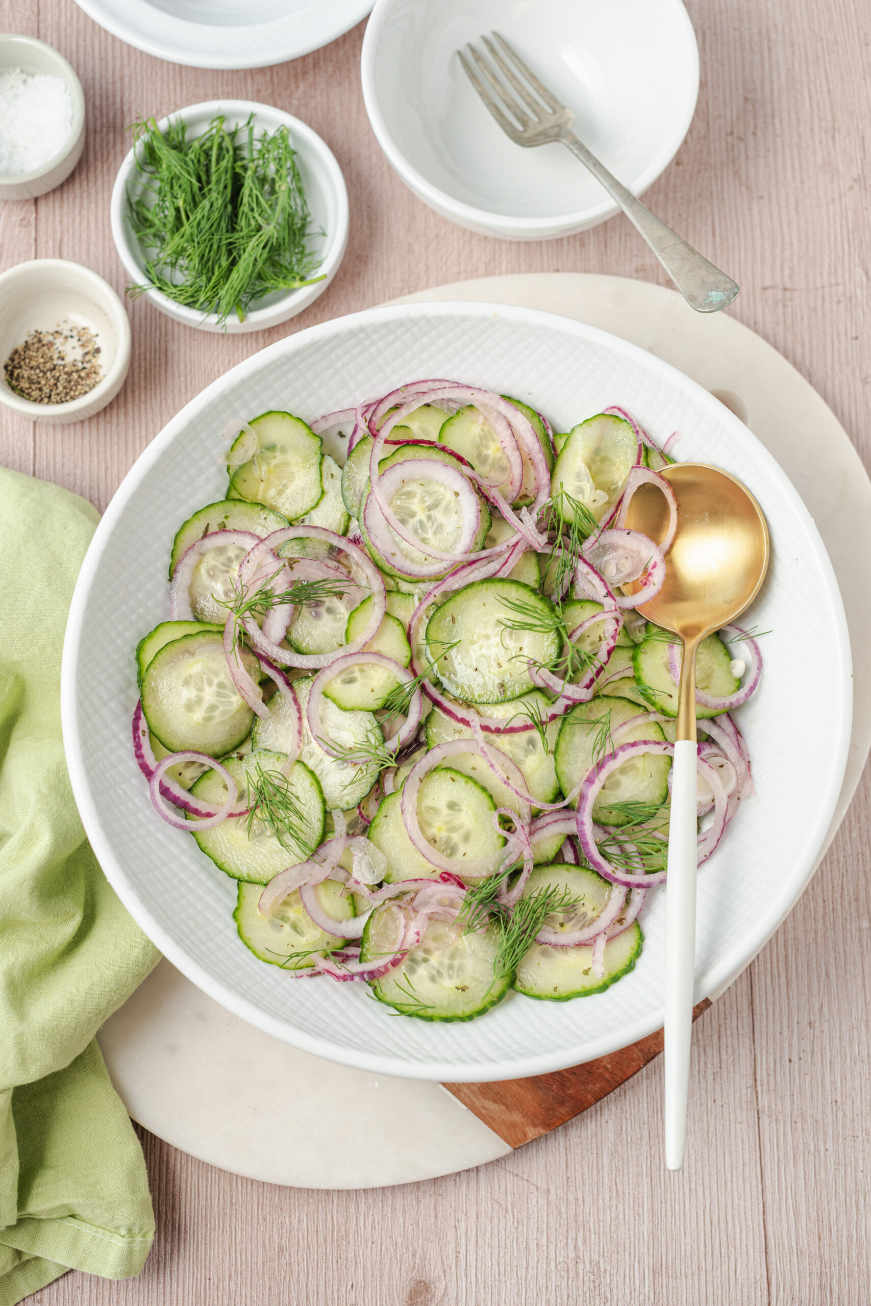 Cucumber and onion salad in a white bowl, garnished with fresh dill.