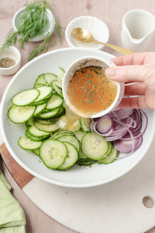 Pouring dressing over sliced cucumbers and red onions for cucumber and onion salad.