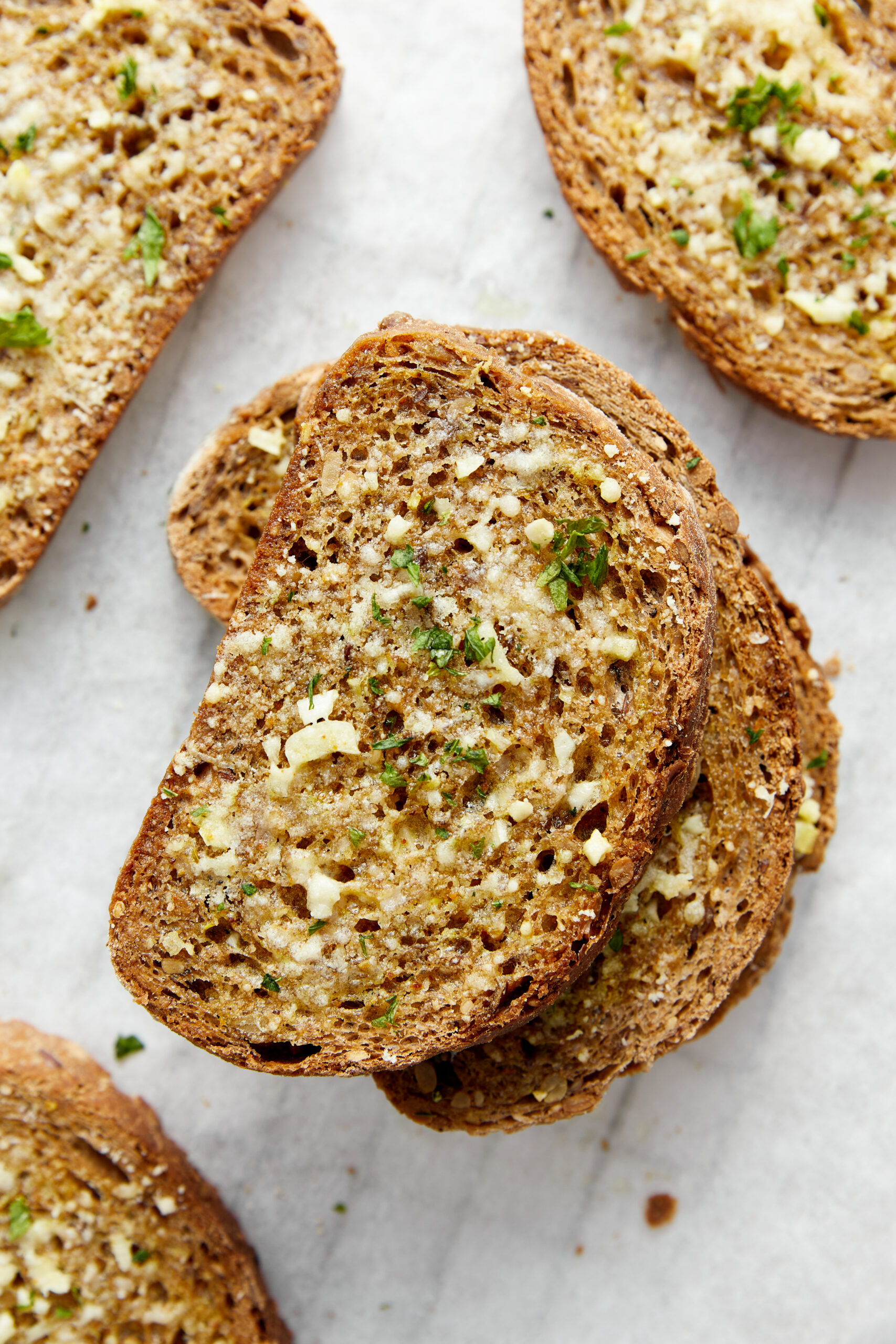 Golden brown slices of garlic toast garnished with fresh parsley on a white surface.
