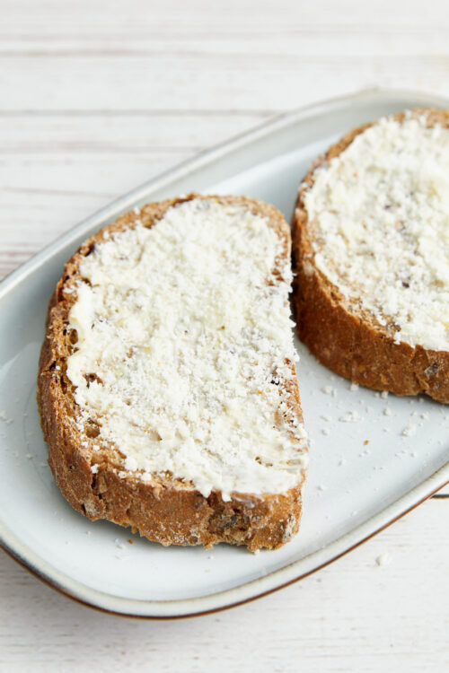 Garlic toast slices topped with Parmesan cheese on a baking tray.