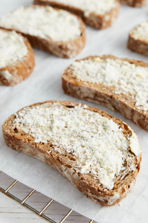 Slices of garlic toast topped with Parmesan cheese on parchment paper.