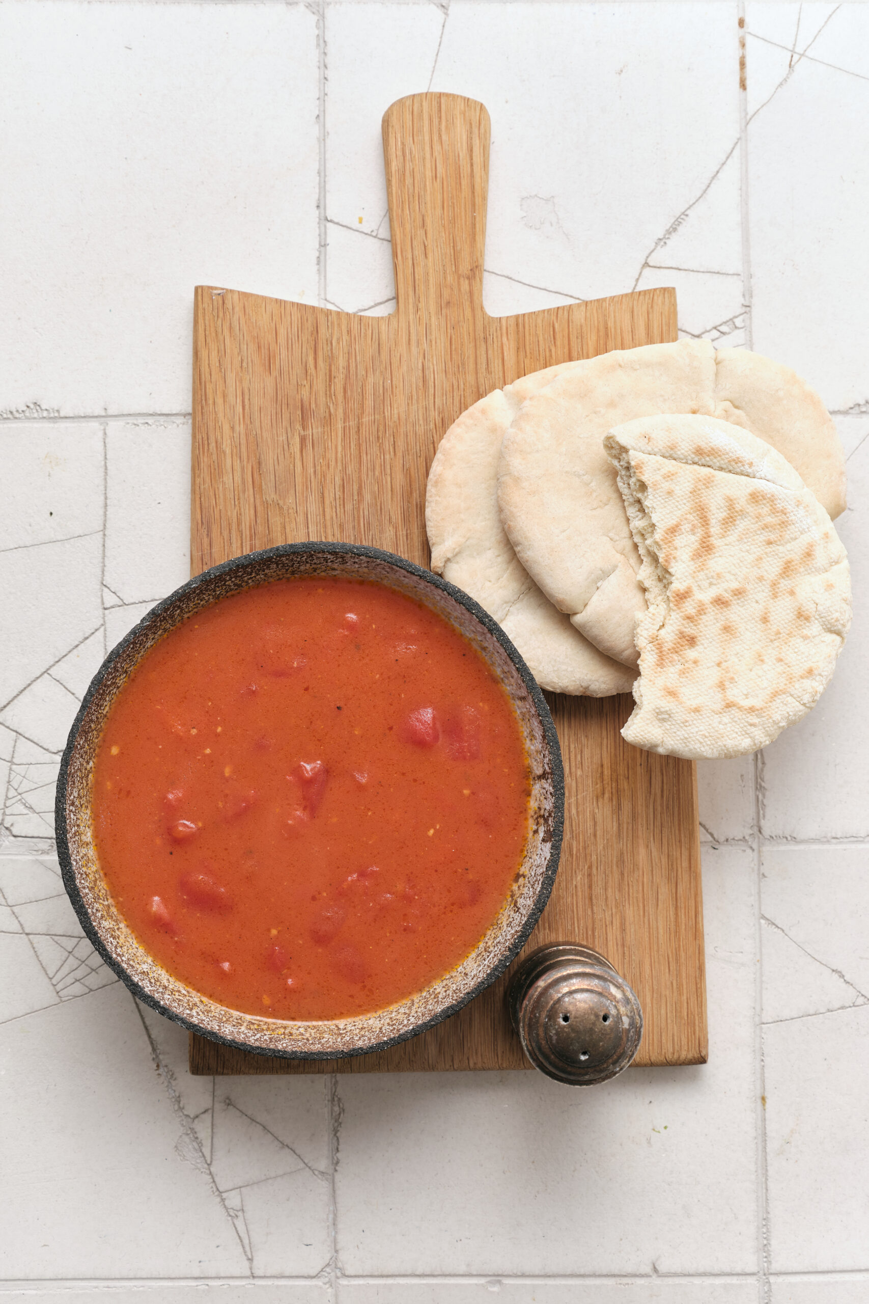 Tomato gravy in a dark bowl, served with pita bread on a wooden cutting board.
