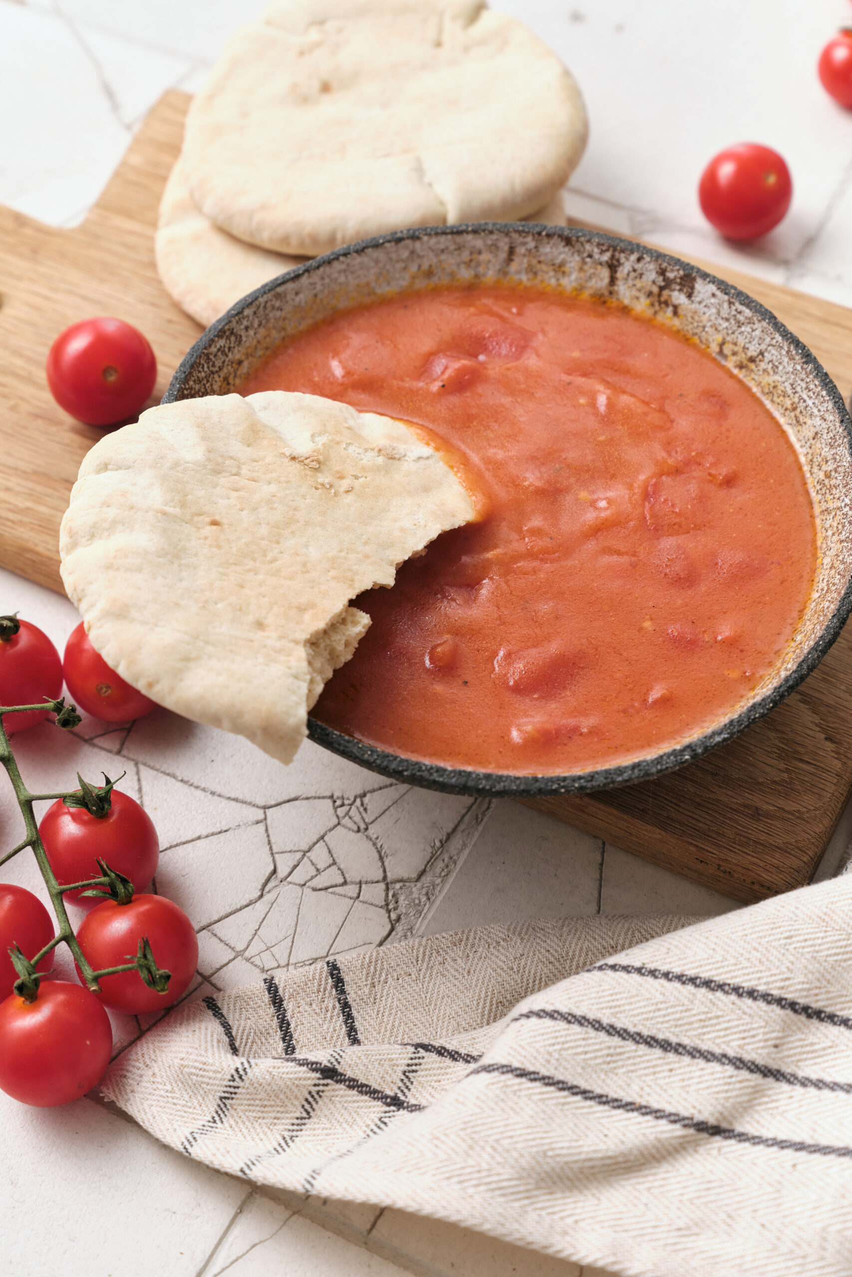Tomato gravy in a dark bowl, served with pita bread and fresh cherry tomatoes.