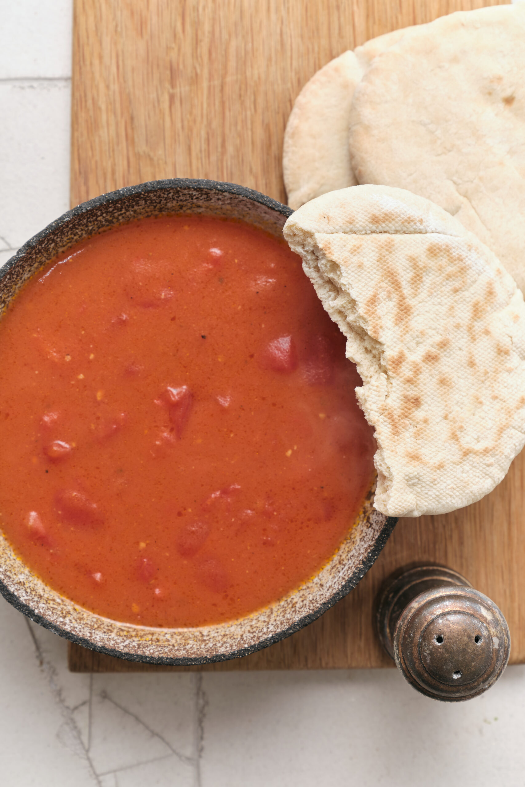 A bowl of chunky tomato gravy with visible diced tomatoes, served with pita bread.