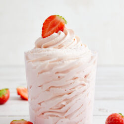 Strawberry whipped cream in a clear glass, garnished with a fresh strawberry half.