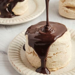 Pouring warm chocolate gravy over a tall biscuit, a classic chocolate gravy and biscuits dish.