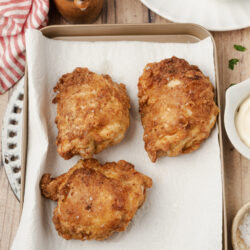 Golden-brown fried chicken pieces draining on paper towels on a baking sheet.